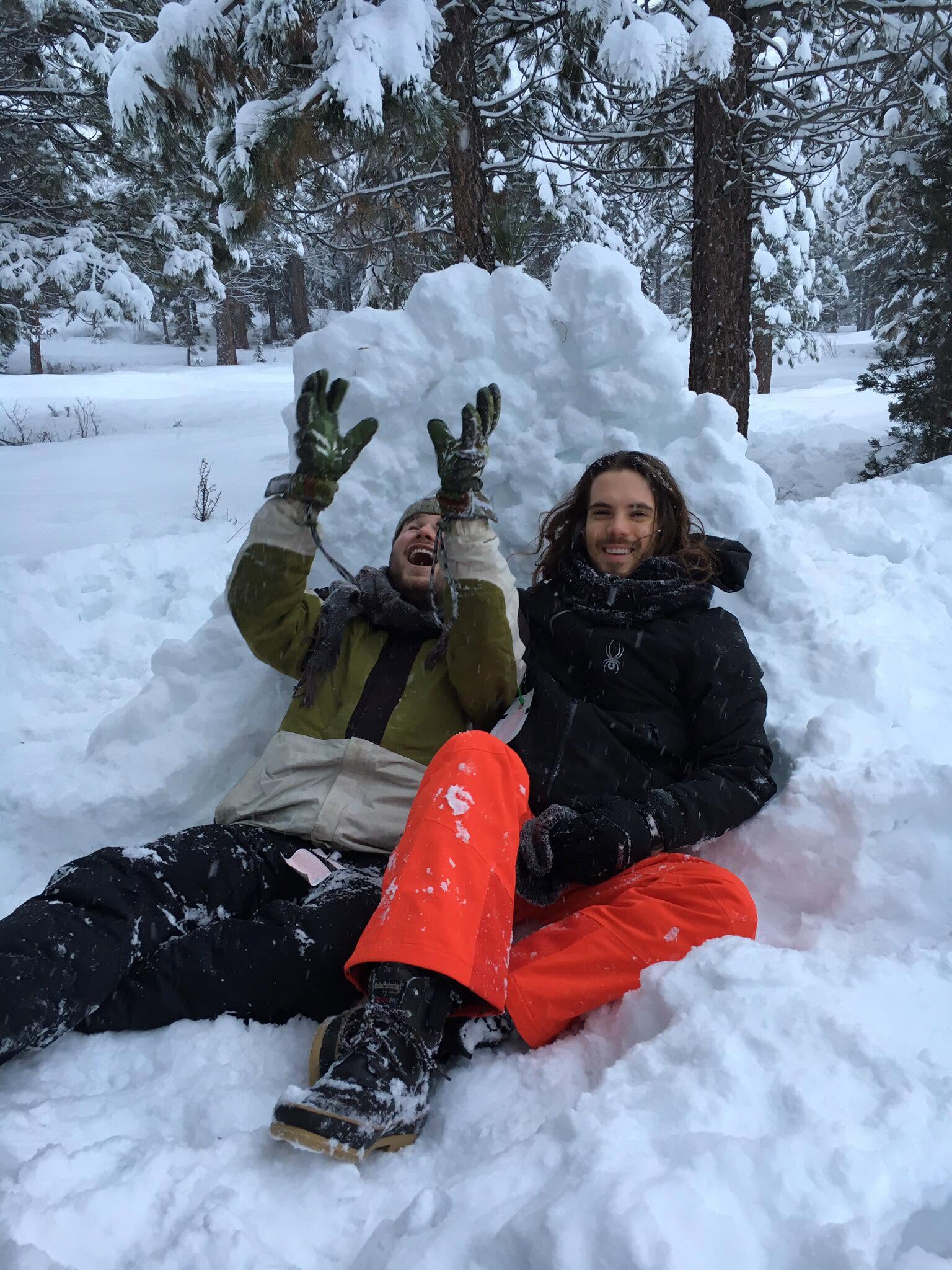 Faust Whale and Robbie seated together in deep snow beneath snow-covered pine trees